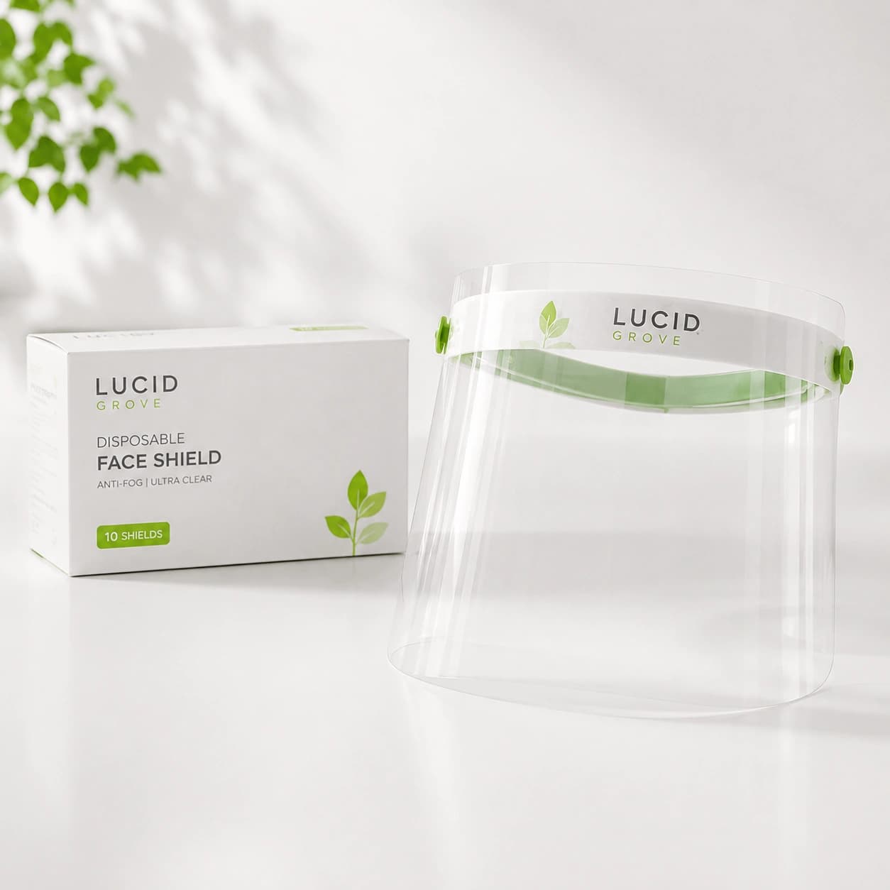 A Lucid Grove disposable face shield with a green brow band, beside its box.