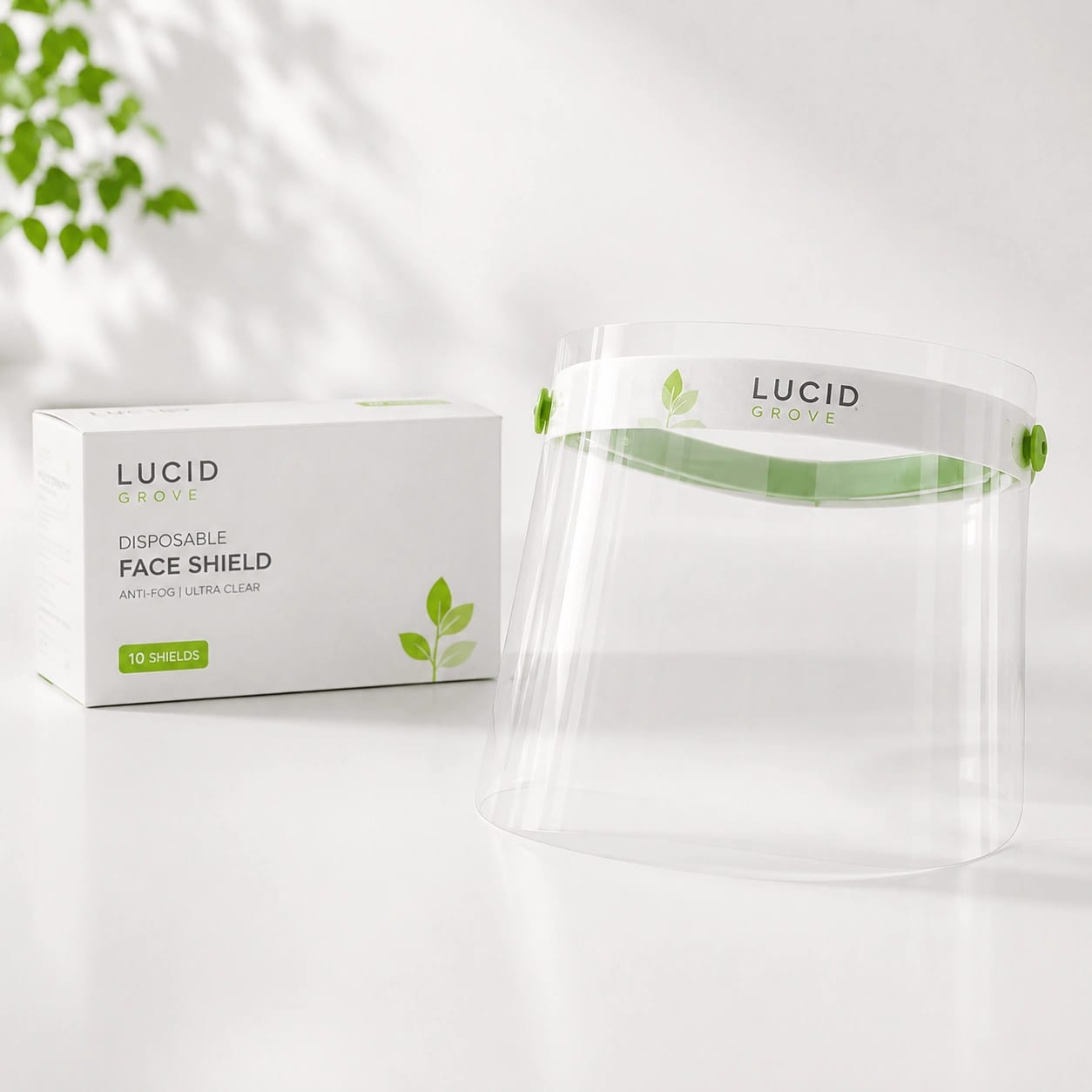 A Lucid Grove disposable face shield with a green brow band, beside its box.